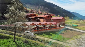 Un edificio tradicional de techo rojo con varios balcones, rodeado de abundante vegetación y montañas al fondo.