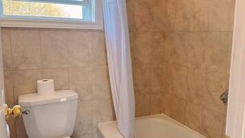 Un baño con inodoro, bañera y ventana con cortina.