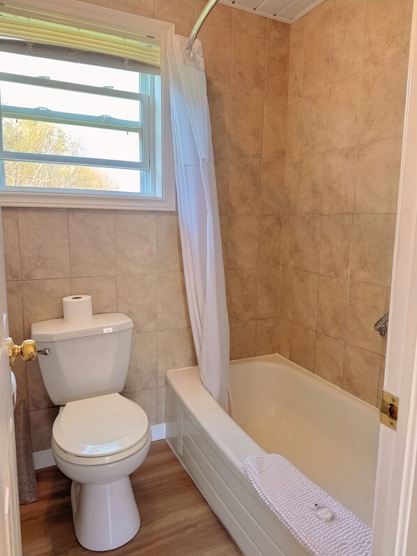 Une salle de bain avec des toilettes, une baignoire et une fenêtre avec un rideau.