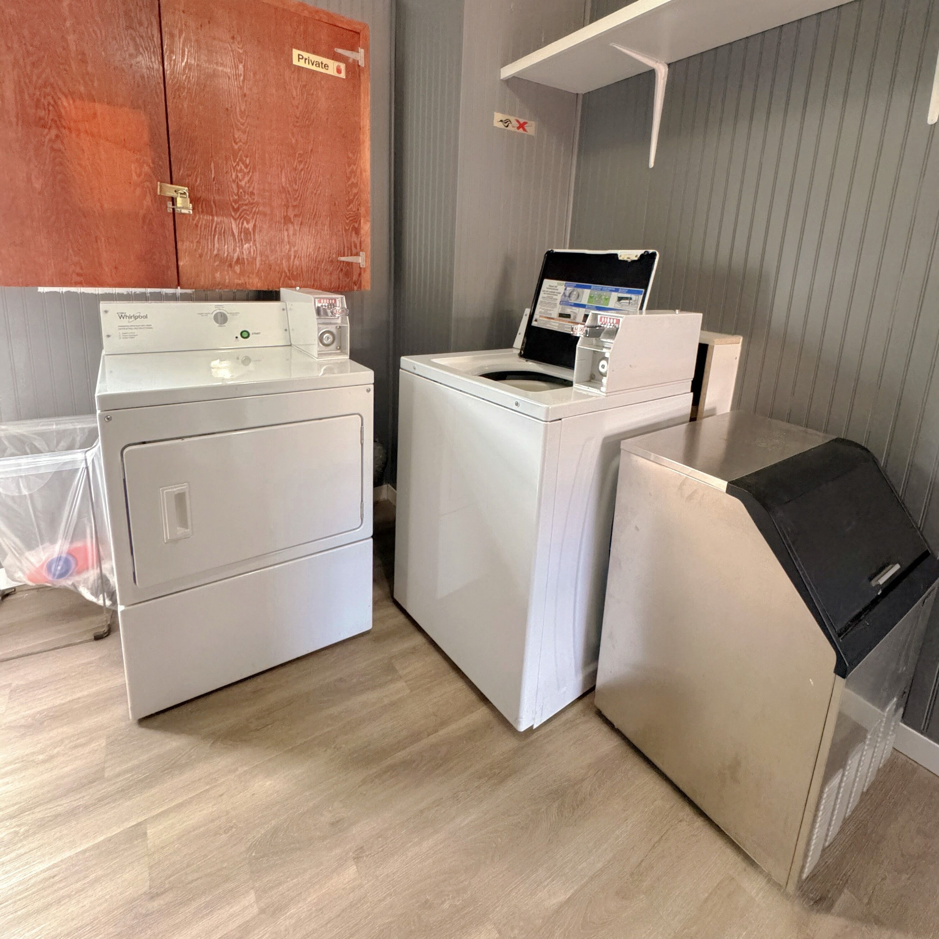 A laundry area with two front-loading washers and a dryer, a wooden cabinet, and a metal shelf.
