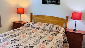 A bedroom with a wooden bed, two bedside tables with lamps, a wall-mounted picture, and a wooden floor.