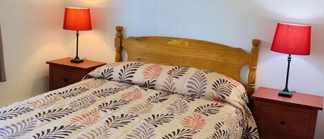 A bedroom with a wooden bed, two bedside tables with lamps, a wall-mounted picture, and a wooden floor.