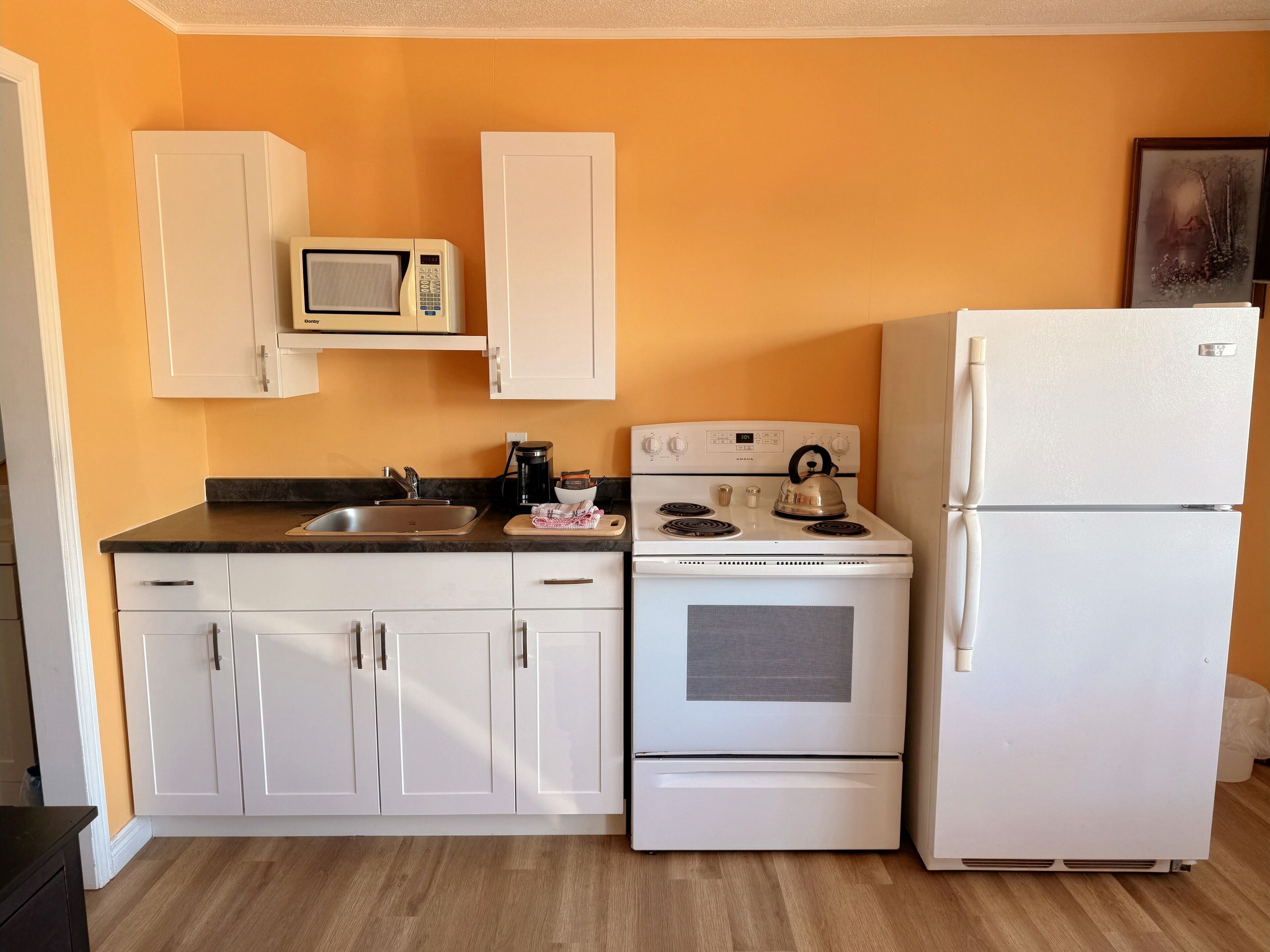 A kitchen with white cabinets, a stove, a refrigerator, and a microwave.