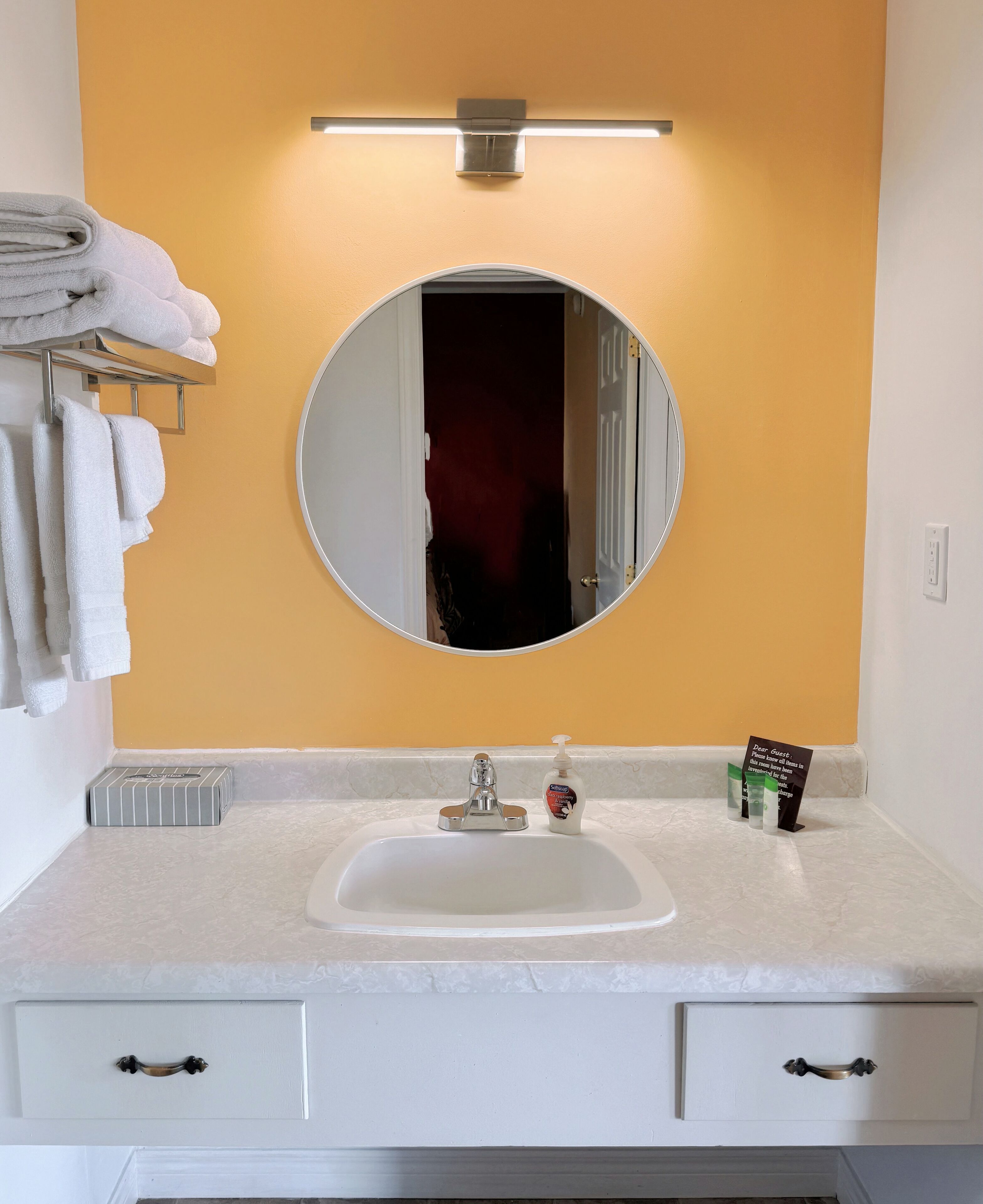 Une salle de bain avec un lavabo blanc, un miroir rond et un porte-serviettes avec des serviettes pliées.