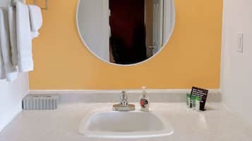 Une salle de bain avec un lavabo blanc, un miroir rond et un porte-serviettes avec des serviettes pliées.