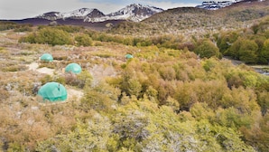 Paisaje montañoso con tres tiendas de campaña abovedadas en un área boscosa.