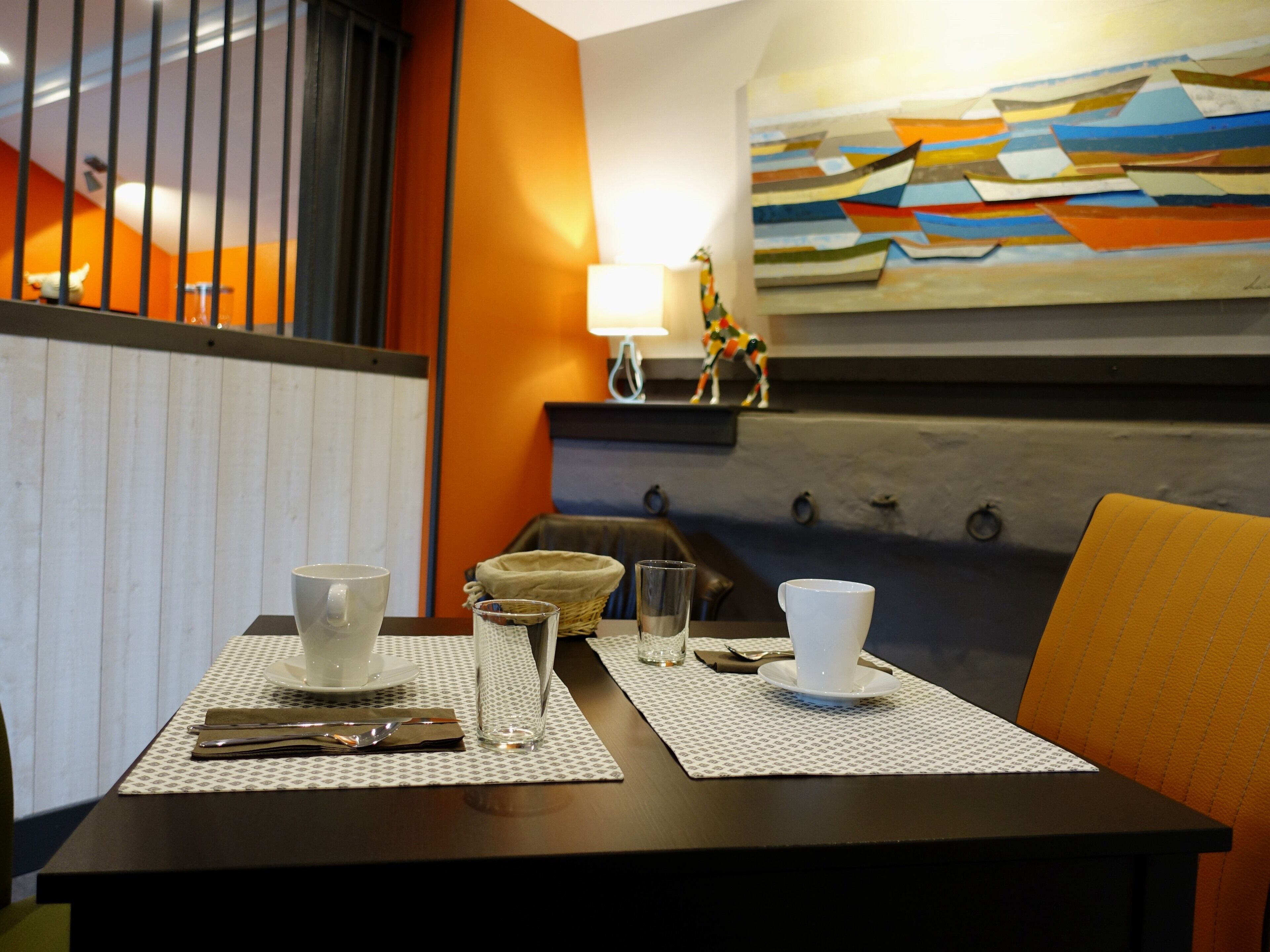 A dining area with a table set for two, featuring a white cup, a glass, a napkin, and a small basket.
