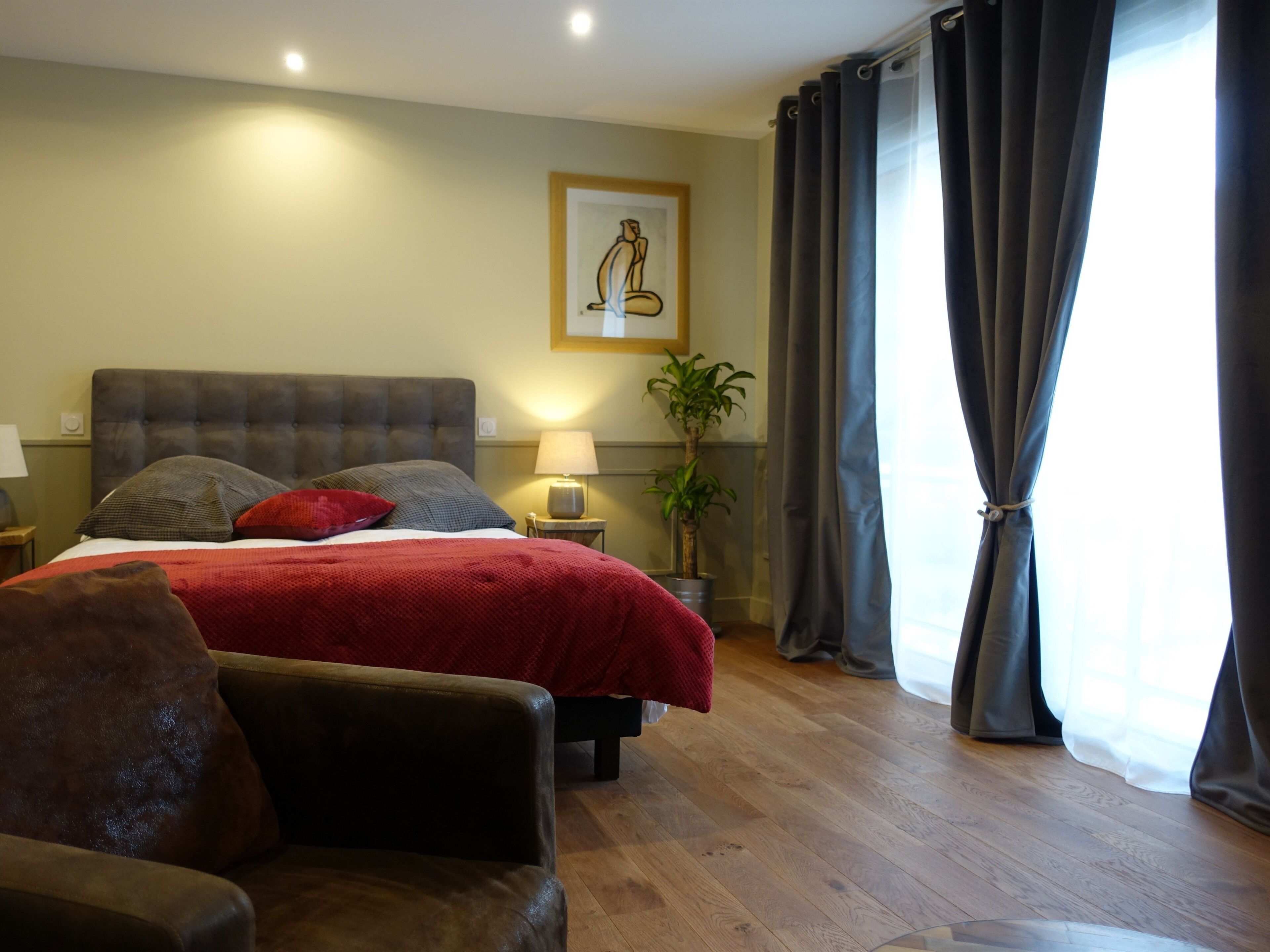 A bedroom with a bed, a nightstand, a lamp, a potted plant, and a window with curtains.