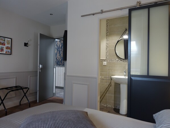 A hotel room with a bed, a bedside table, a bathroom with a sink and mirror, and a door leading to another room. - Les Prémontrés (Falaise)
