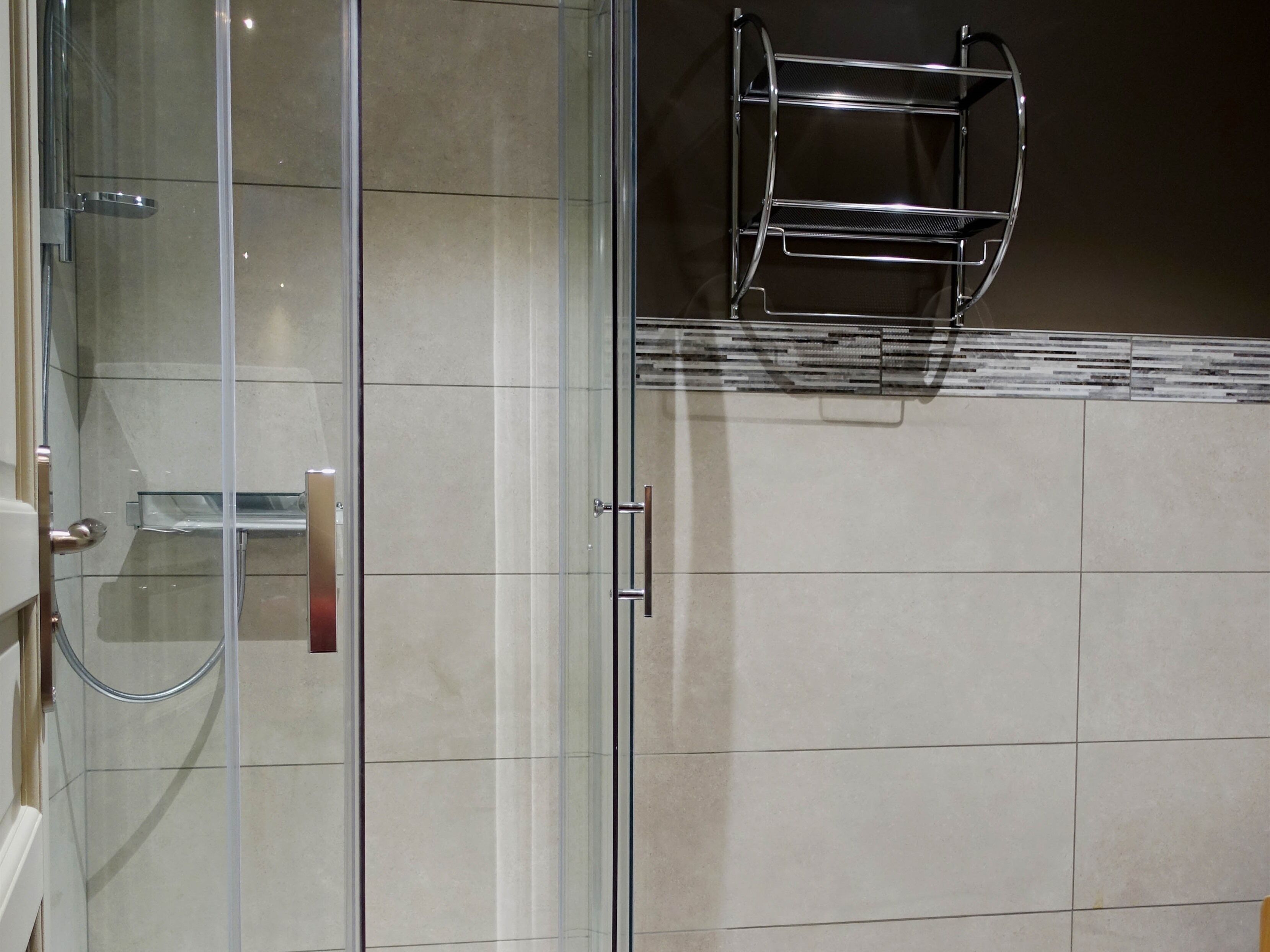 A glass-enclosed shower with a chrome faucet and a towel rack mounted on the wall.