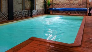 Una piscina interior amb un solàrium de fusta i parets de rajoles amb disseny.
