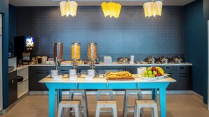 A modern kitchen with a blue island, white stools, and a television in the background.