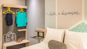 Habitación de hotel con una cama, una mesita de noche con un zapato, un escritorio pequeño y una pared con un diseño geométrico y una frase motivadora.