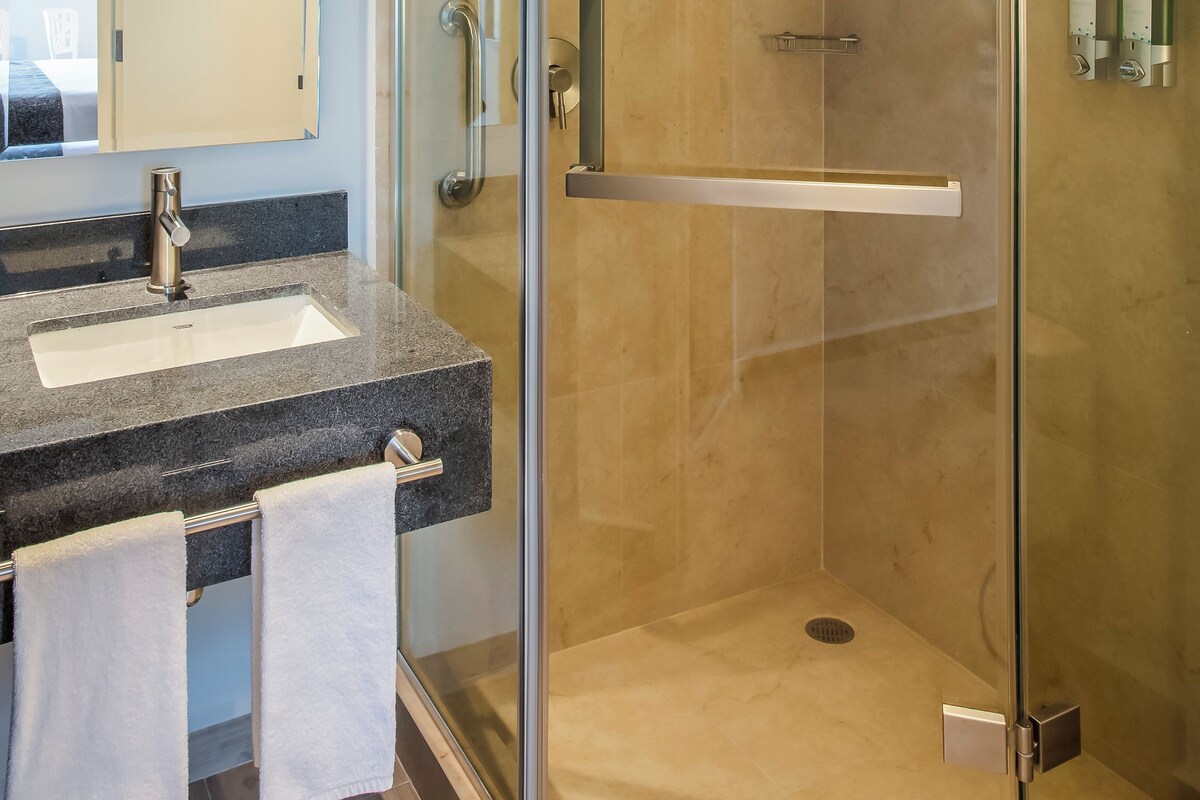 Un baño moderno con ducha envuelta en vidrio, lavabo con encimera de mármol y espejo.