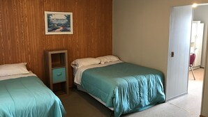 A room with two beds, a wooden wall, a small cabinet, and a door leading to another room. - The Landing on the Wolf (Winneconne)