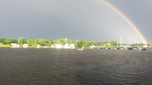 A river with a rainbow arching over it, a bridge in the background, and buildings along the riverbank. - The Landing on the Wolf (Winneconne)