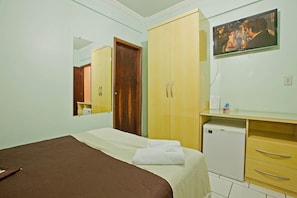 A bedroom with a bed, a wardrobe, a small refrigerator, and a television on the wall.