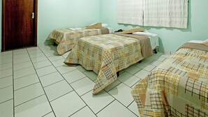 Habitación de hotel con tres camas, cada una con colcha a cuadros, una puerta de madera y una pared verde claro.
