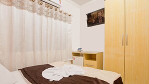 Un dormitorio con cama, un armario de madera, un escritorio pequeño con silla y un televisor montado en la pared.