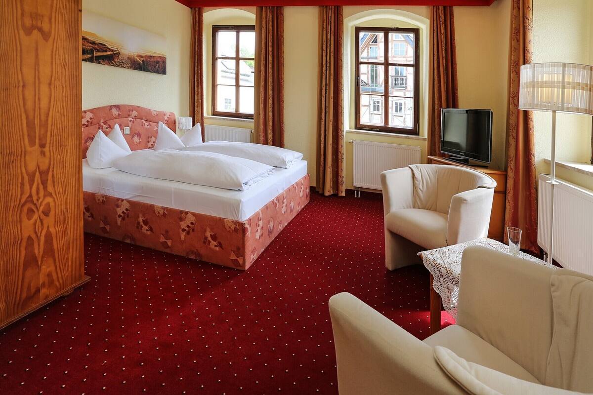A hotel room with a bed, a TV, a chair, and a window with curtains.