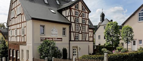 A traditional half-timbered building with a sign reading "30 Wohnzimmer Herzlich Willkommen" and a weather vane on the roof.