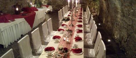 A long banquet table set for a formal event in a stone-walled room.