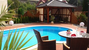 A swimming pool with wicker chairs and a table set for dining, surrounded by a garden and a gazebo. - Landhotel Thürmchen (Schirgiswalde-Kirschau)