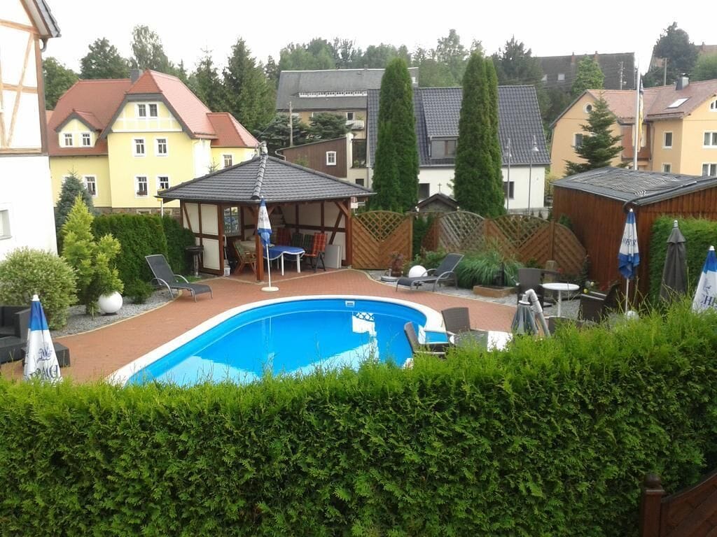 En privat trädgård med en pool, solstolar, en möblerad uteplats under tak och ett trästaket.