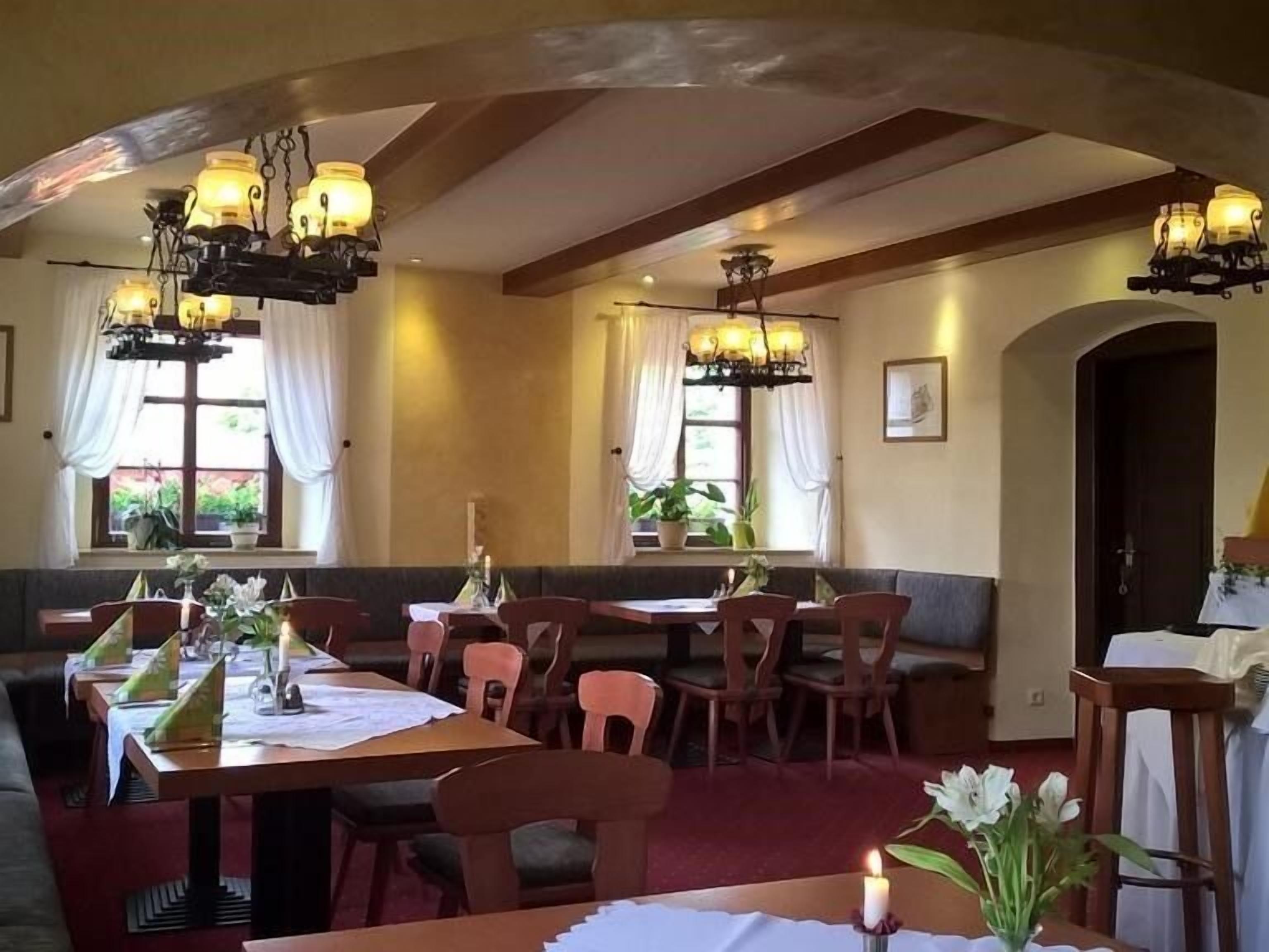 Un restaurant avec des tables et des chaises en bois, des lustres et de grandes fenêtres ornées de rideaux.