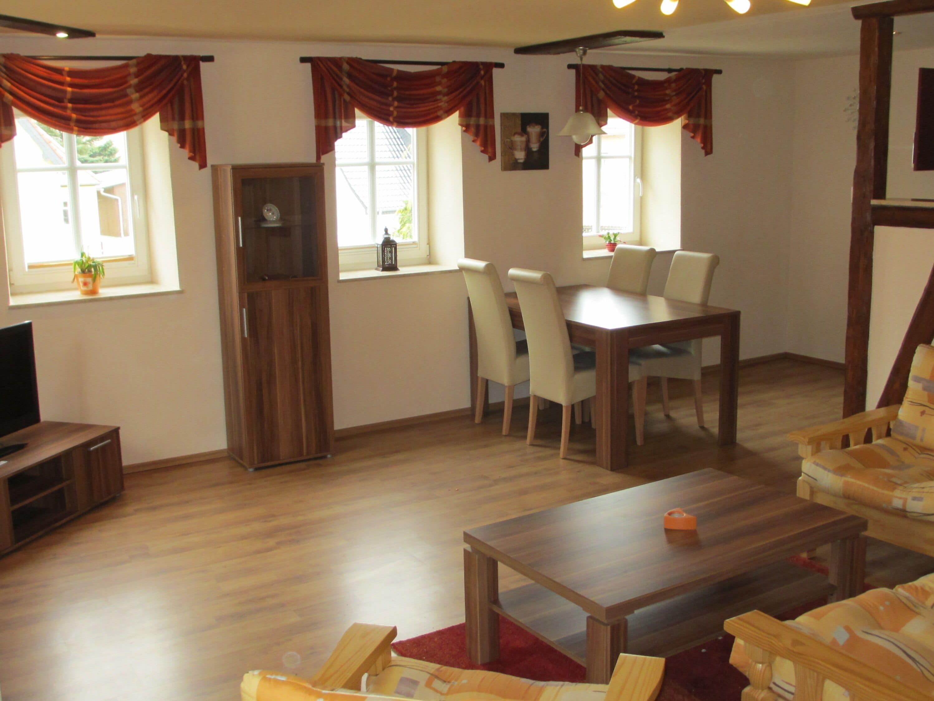 A living room with a wooden table, chairs, a sofa, a TV, and a cabinet.