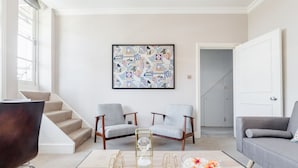 A modern living room with a staircase, two grey armchairs, a grey sofa, and a large abstract painting on the wall. - Kensington Apartment with terrace (London)