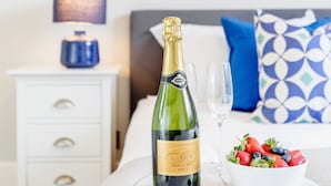 A bed with a white headboard, a bedside table with a blue lamp, a bottle of champagne, a glass, and a bowl of fruit on a white tray. - Kensington Apartment with terrace (London)