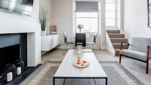 A modern living room with a fireplace, a dining area with a table and chairs, and a staircase leading to another floor. - Kensington Apartment with terrace (London)