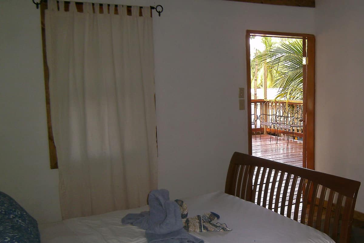 Une chambre à coucher comprenant un lit, une chaise, un rideau et une porte donnant sur un espace extérieur.