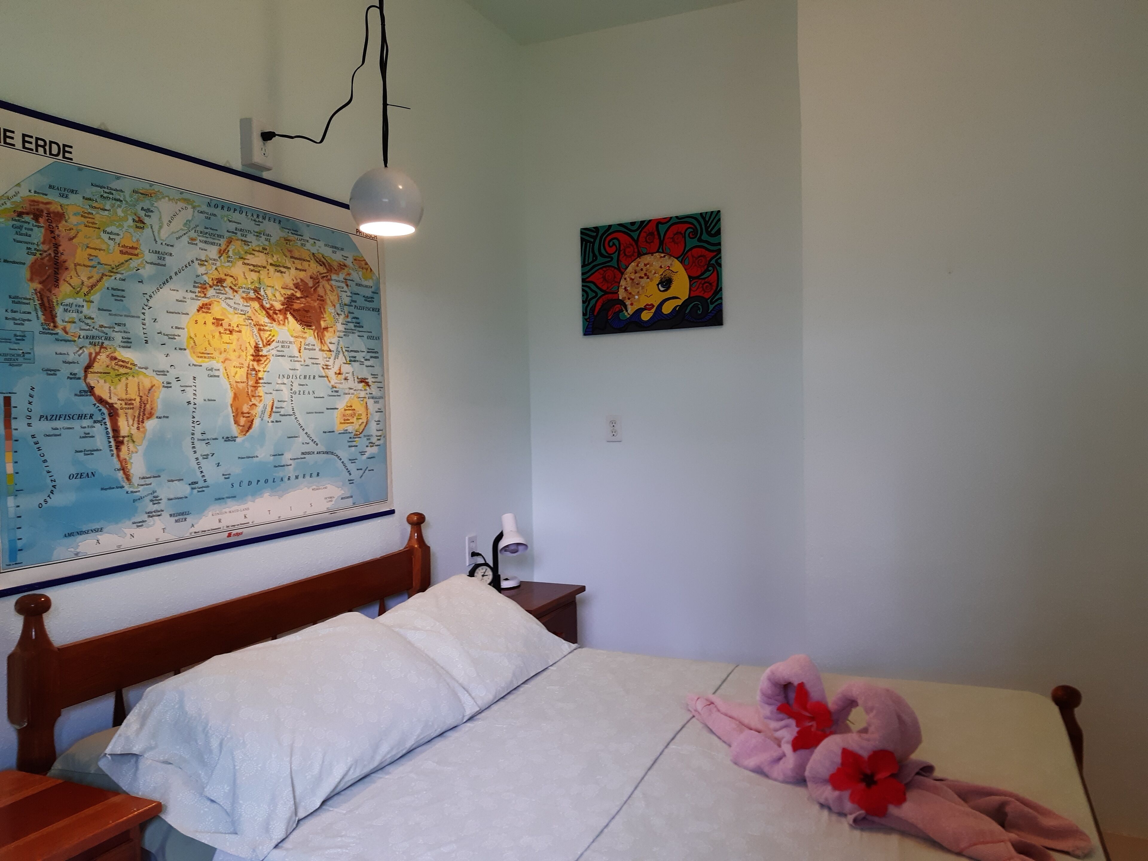 Un dormitorio con una cama, un mapa del mundo, un cuadro y una lámpara.