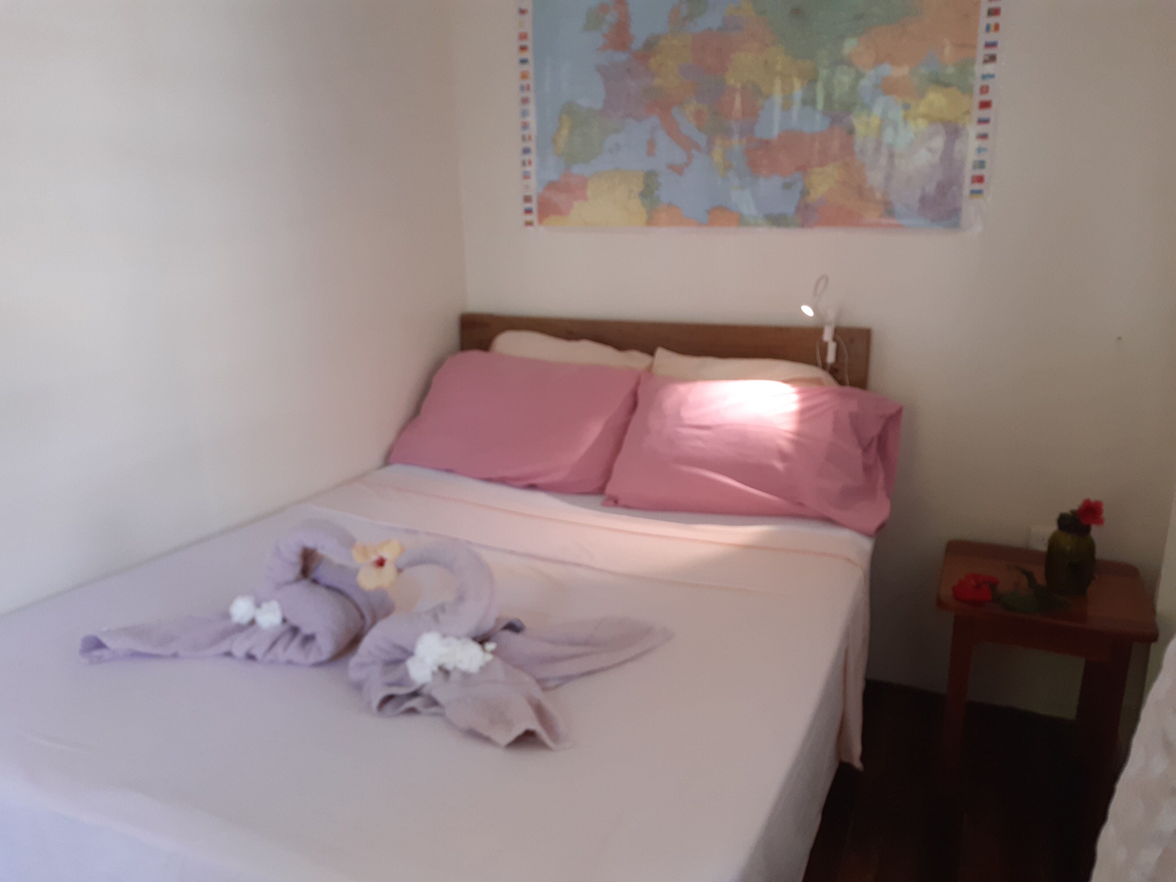 Una cama bien hecha con ropa de cama rosa y una decoración de toallas.