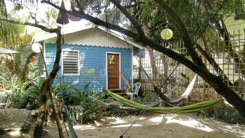 Una casa azul con puerta de madera, rodeada de follaje y una hamaca.