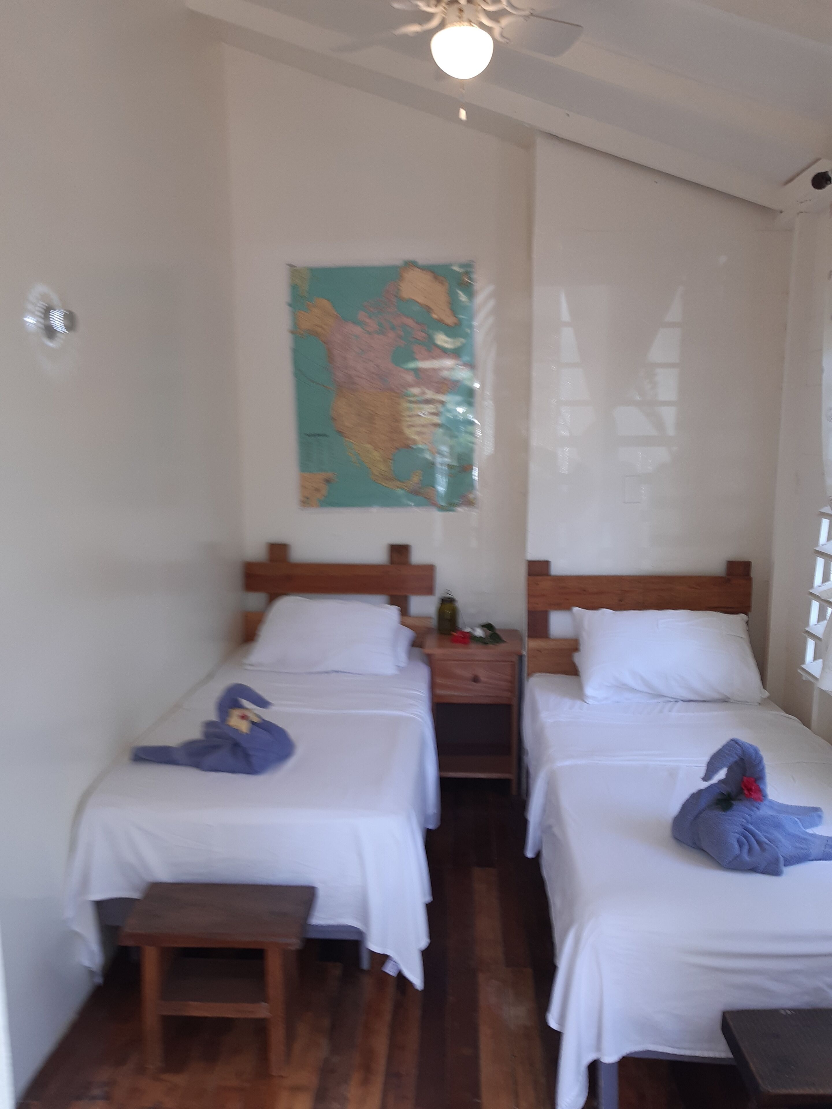 A room with two single beds, a wooden nightstand, a small table, and a map on the wall.