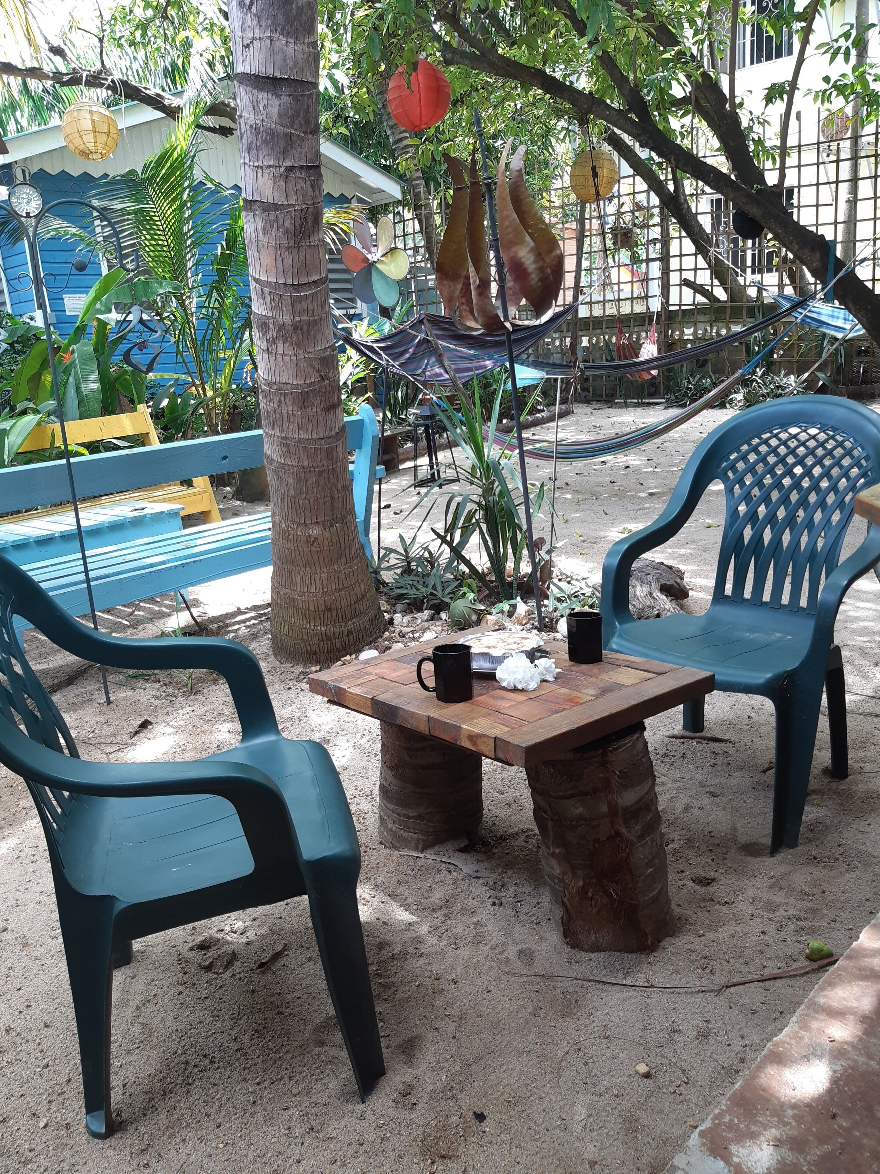 Une table en bois, des chaises et un hamac dans un coin du jardin.