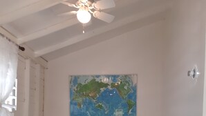 Una habitación con dos camas, suelo de madera, ventilador de techo, un mapa del mundo en la pared y una mesita entre las camas.