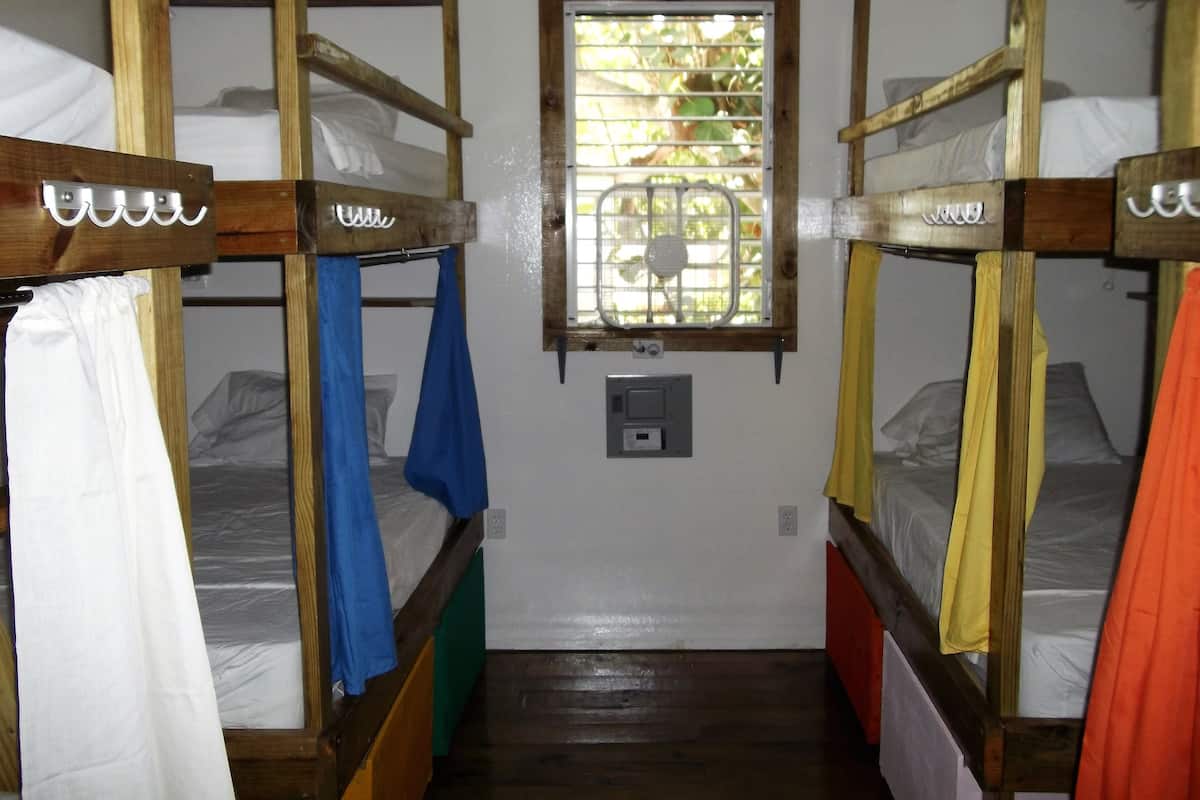 Une chambre de dortoir avec des lits superposés, une fenêtre grillagée et une prise électrique sur le mur.