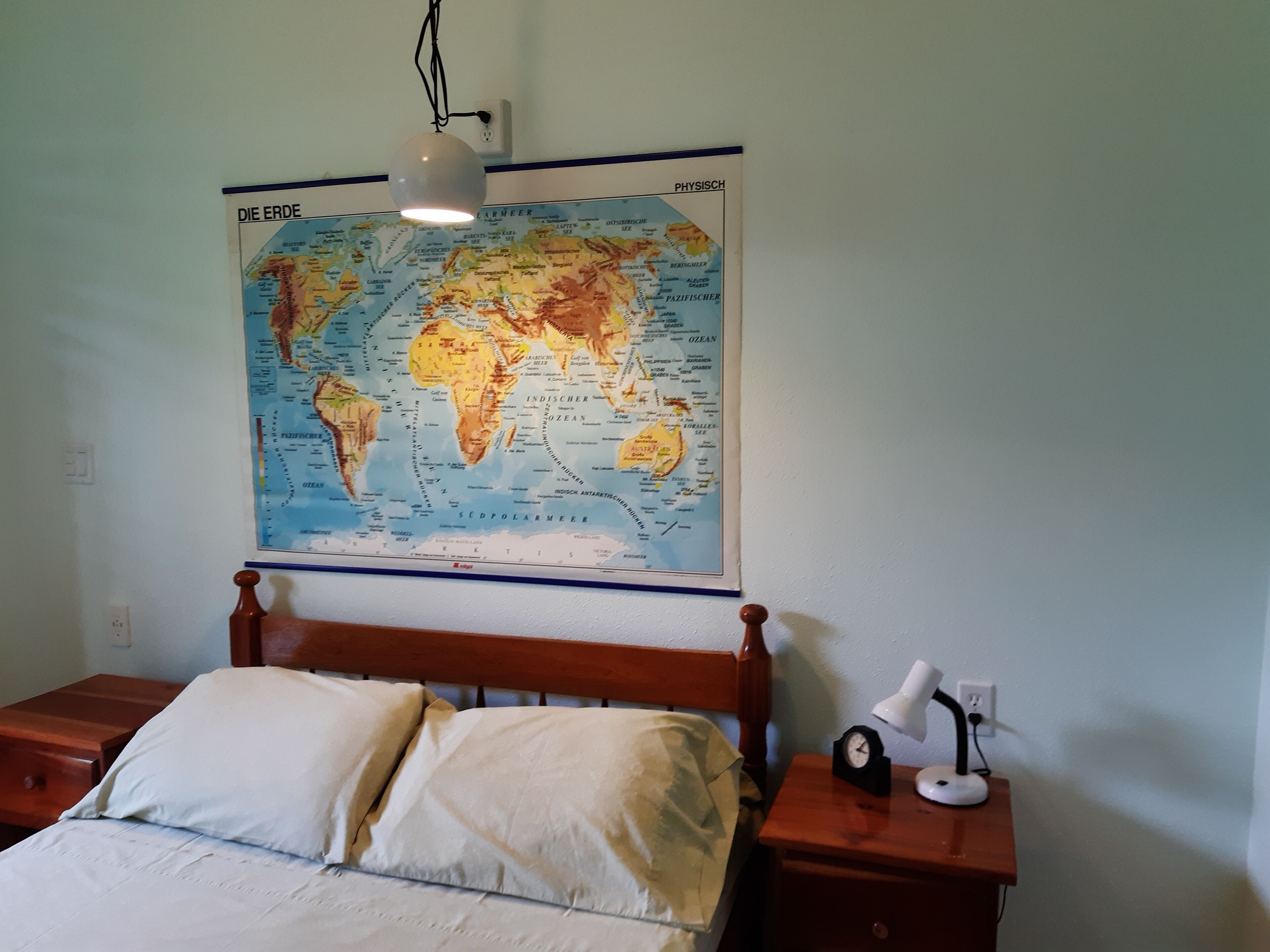 Een slaapkamer met een houten bed, een nachtkastje met een lamp en een wereldkaart aan de muur.