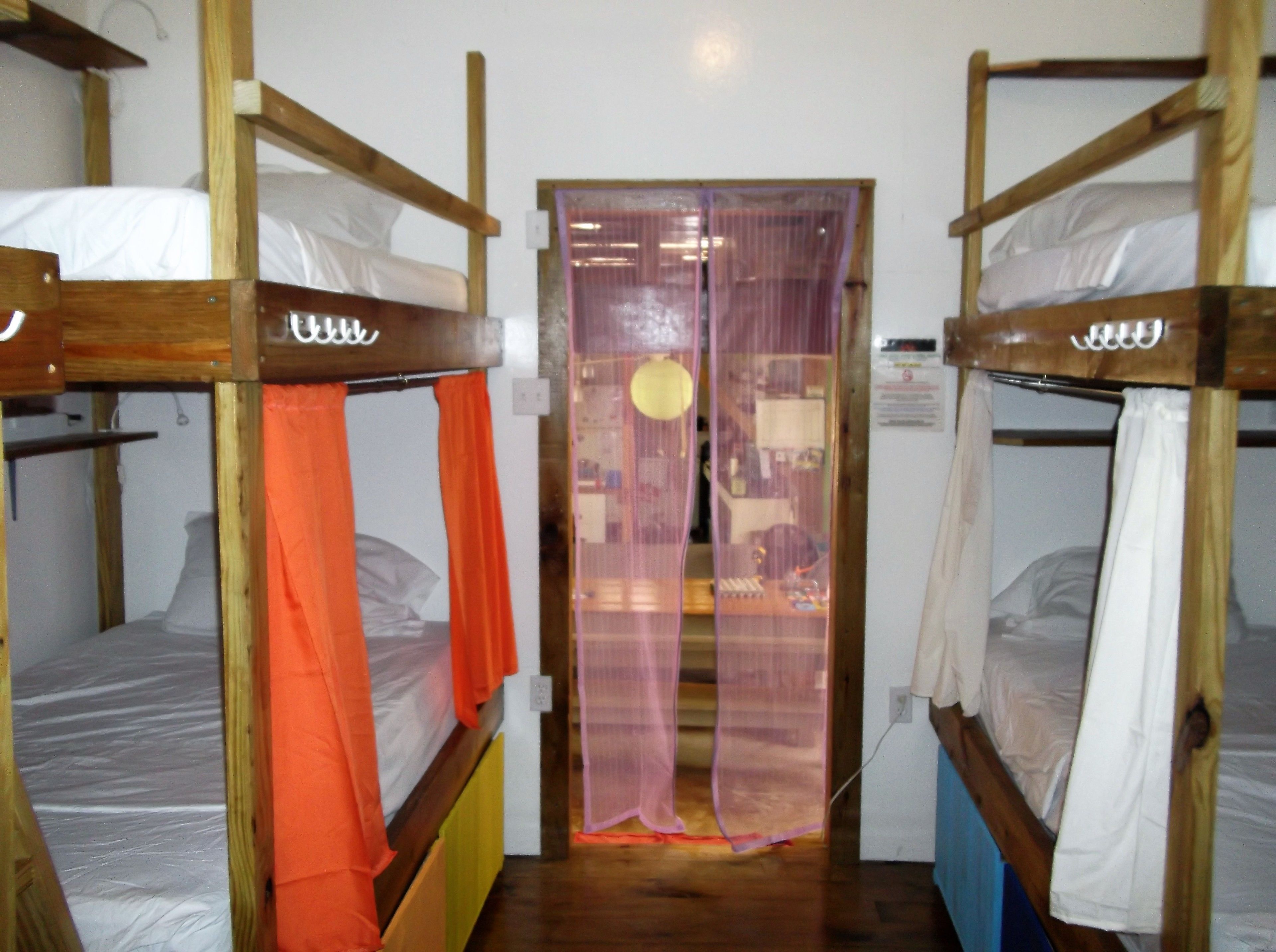 Una habitación con literas, una puerta con cortina y una mesita con lámpara.