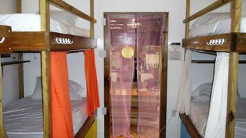 A room with bunk beds, a door with a curtain, and a small table with a lamp.