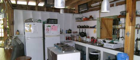 A rustic kitchen with wooden beams, a refrigerator, a stove, and various kitchen utensils.