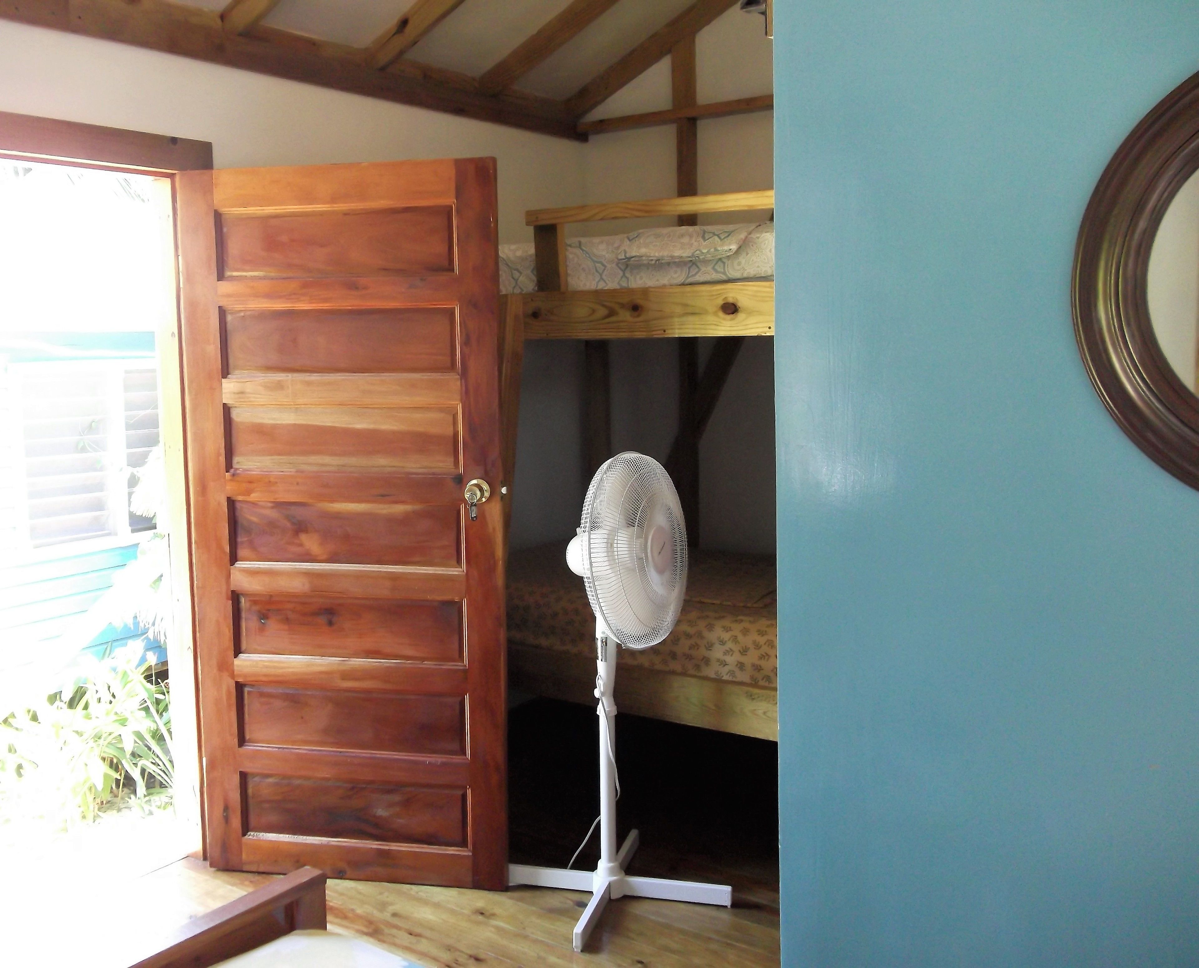 A room with a wooden door, a bunk bed, and a standing fan.