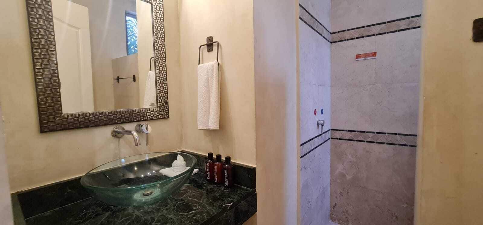 Ein Badezimmer mit einem Waschbecken aus Glas, einem großen Spiegel, einem Handtuchhalter und einer Duschkabine.