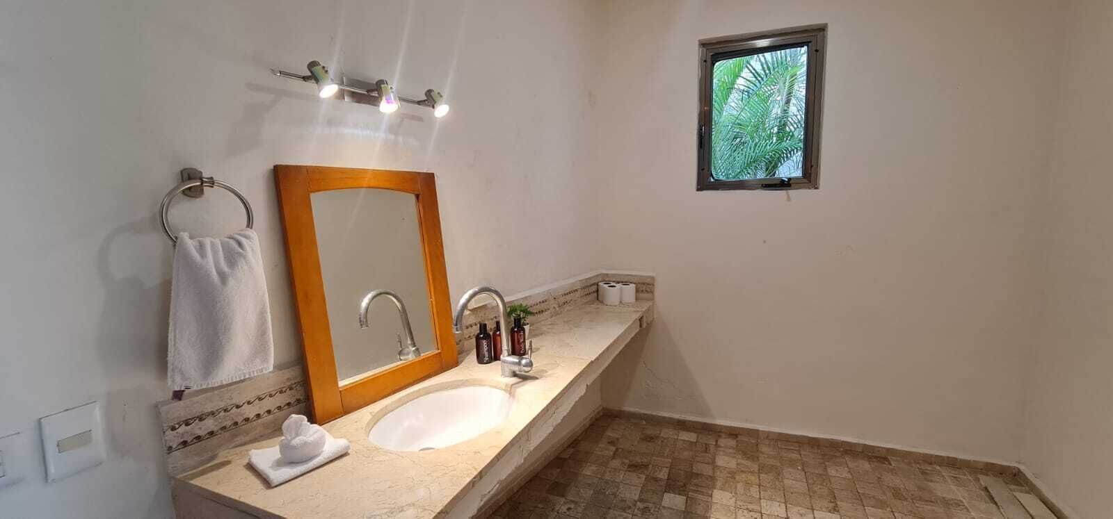 Ein Badezimmer mit Waschbecken, Spiegel, Handtuchhalter und einem kleinen Fenster mit Blick auf Palmen.