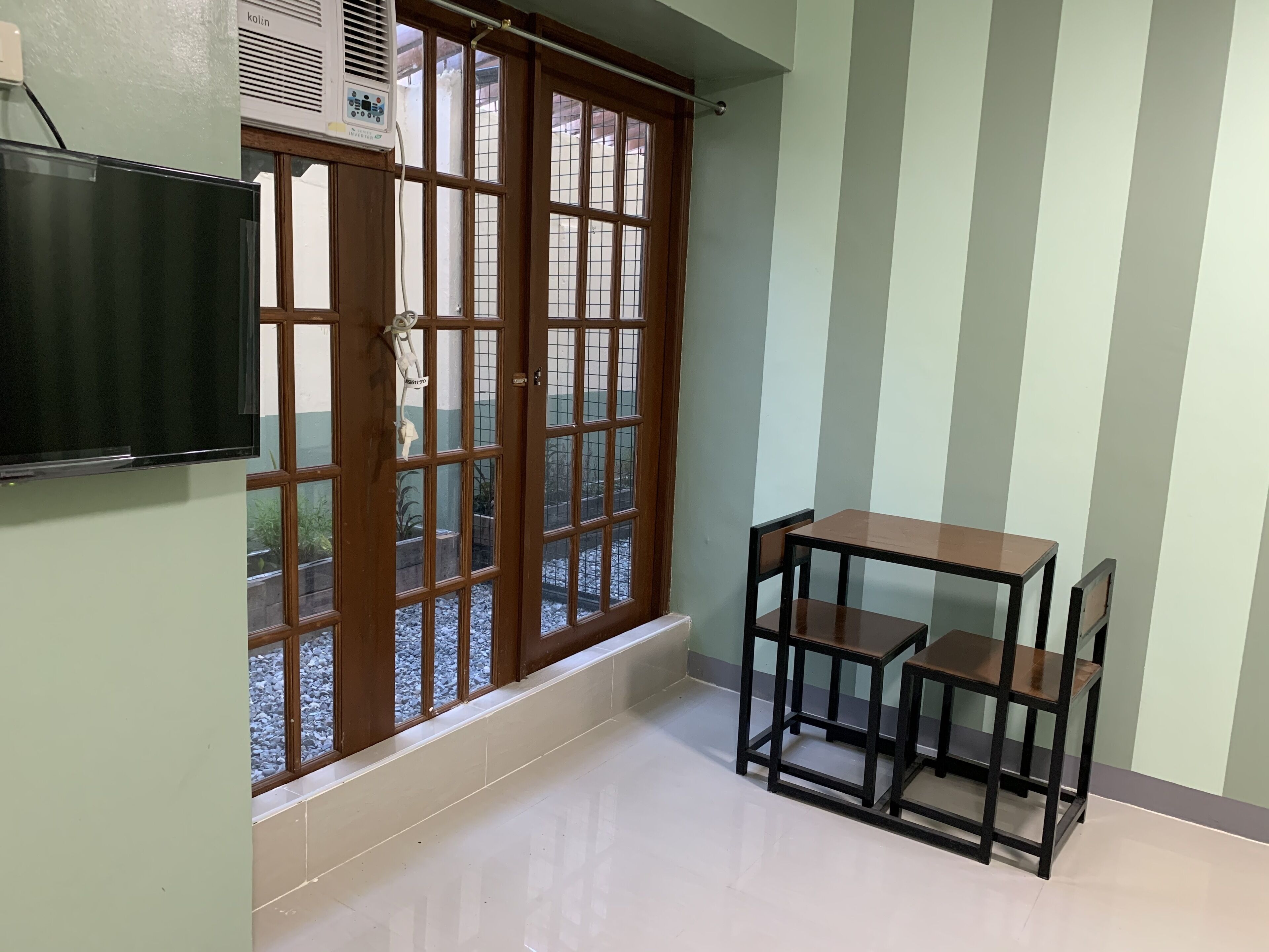 Una habitación con un gran ventanal corredera, un televisor de pantalla plana montado en la pared y una pequeña mesa de madera con dos sillas.