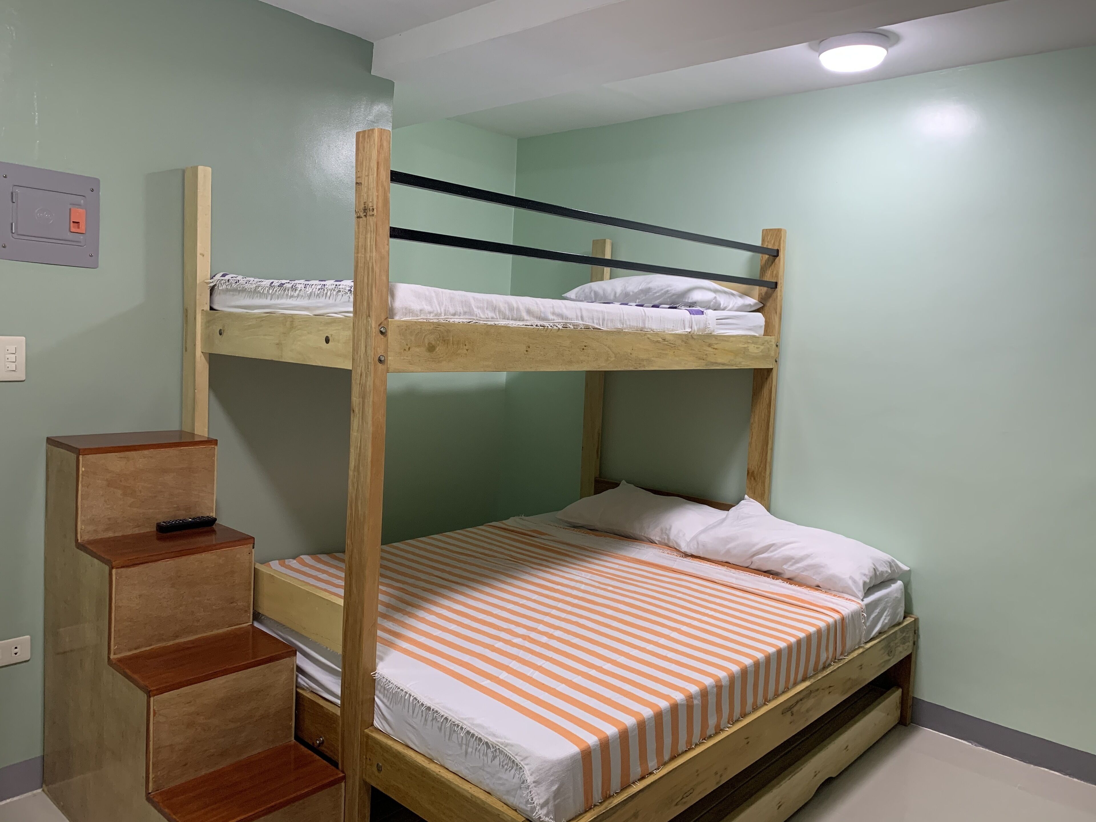 A bunk bed room with a wooden ladder, a small wooden cabinet, and a light switch on the wall.